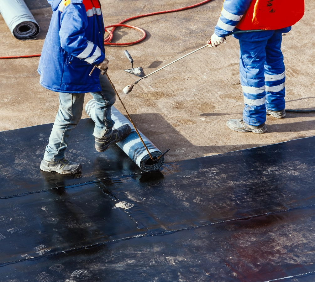 Workers installing waterproofing on a flat roof.
