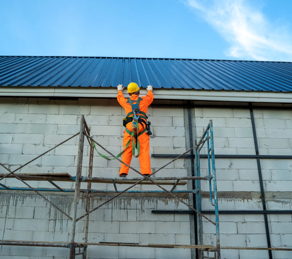 Worker on scaffolding installing metal roof.